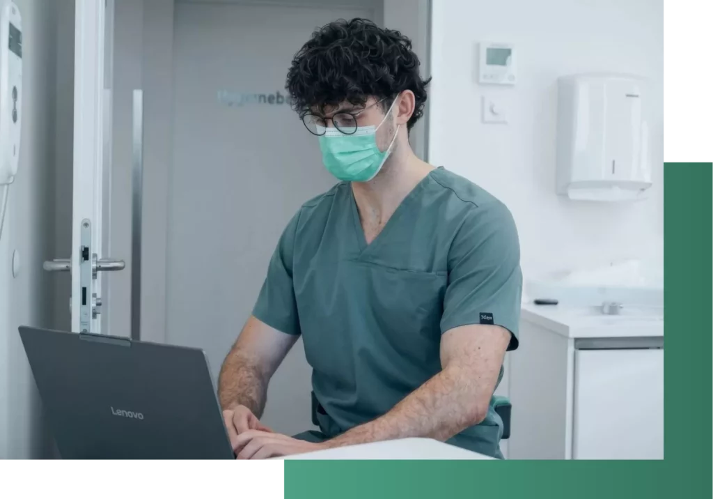 Arzt arbeitet am Laptop, trägt Maske.